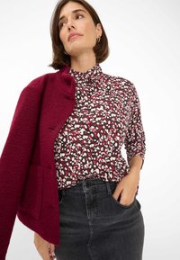 Gestructureerde bordeauxrode trui over een gegolfde blouse met crème en donkerbordeaux vlekken, gecombineerd met een aansluitende zwarte denim rok.