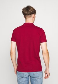 Polo bordeaux à manches courtes, en coton, avec un col classique et une coupe ajustée, associé à un jean bleu.