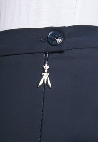 Pantalone od tamnoplave tkanine s glatkom teksturom, koji imaju dugme za zatvaranje i dekorativni srebrni ziper oblikovan kao list.