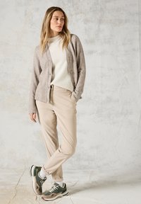 Cardigan beige sopra un maglione bianco a coste, abbinato a pantaloni beige e sneakers verdi. Texture morbide, palette di colori delicata e design semplice.