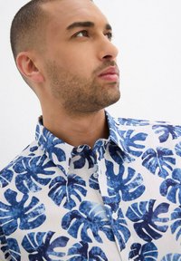 Camicia a maniche corte con sfondo bianco e audaci motivi di foglie tropicali blu. Realizzata in tessuto leggero, con colletto classico e bottoni.