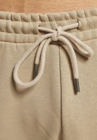 Beige sweatpants met een elastische tailleband, voorzien van een trekkoord met metalen uiteinden, en een gladde, gestructureerde stof.