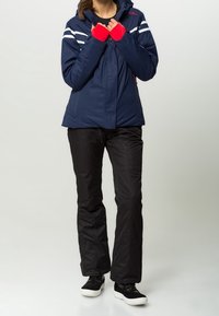 Chaqueta aislante azul marino con rayas blancas, pantalones negros y guantes rojos. Cuenta con capucha, cierre de cremallera y diseño deportivo. Zapatos negros con suelas blancas.