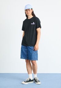 Sort bomulds T-shirt med lilla grafik, blå denim cargo shorts, hvide ankelstrømper og sorte canvas sneakers med hvide såler og snørebånd.