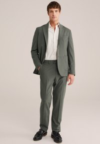 Helles grünes Anzug mit strukturierter Oberfläche, einreihiger Blazer und gerades Bein Hosen, kombiniert mit einem weißen Hemd und schwarzen Schuhen.