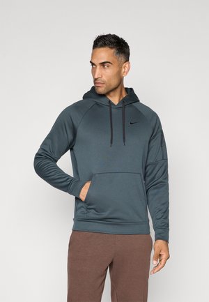 Hanorac de culoare gri închis, fabricat dintr-un material neted, având o buzunar frontal, șnururi și un mic logo pe piept. Este asortat cu pantaloni maro.