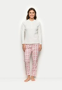 Bílé tričko s dlouhým rukávem a knoflíkovou légou, které je spárováno s červenými a bílými pyžamovými kalhotami s motivem srdcí a cukrových holí. Hladká textura.