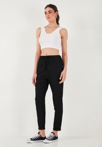 Zwarte drawstring broek met een ontspannen pasvorm en cuffed hems, gecombineerd met een strakke witte geribbelde crop top en zwarte sneakers.