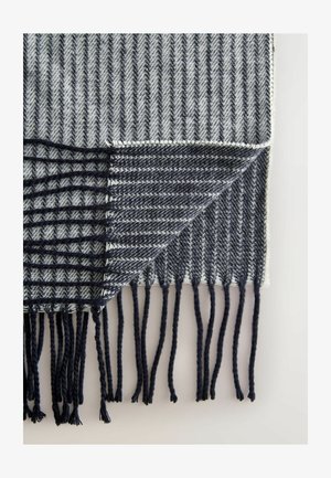 Audimas antklodė su žuvų kaulų raštu pilkos ir tamsiai mėlynos spalvos, su pūkuotais kraštais ir skirtingomis tekstūromis kiekvienoje pusėje.