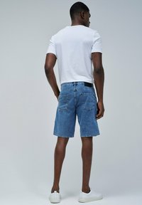 Shorts de mezclilla en azul claro, con un corte recto, bolsillos traseros y una cintura negra. Combinados con una camiseta blanca simple y zapatillas blancas.