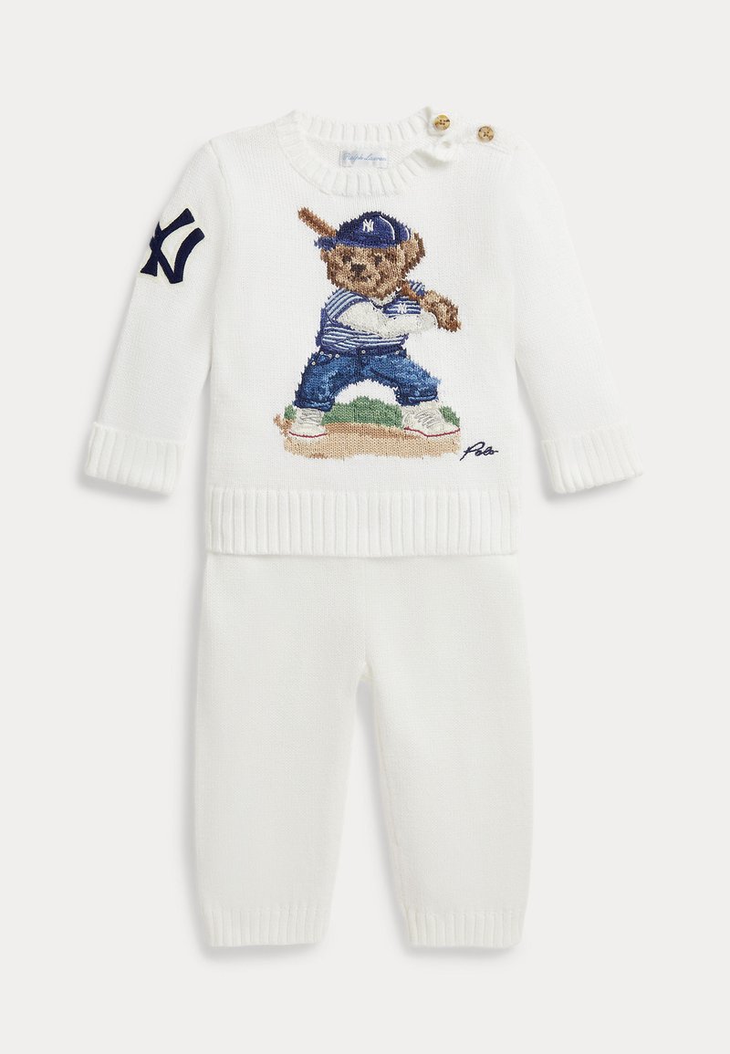 Ensemble pull et pantalon blanc pour bébé avec un ours en peluche tricoté portant un uniforme de baseball et une casquette tenant une batte sur le devant du pull.