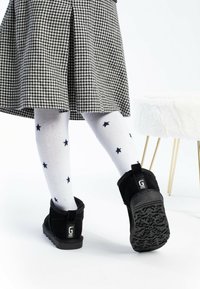 Botas de tobillo de ante negro con una suela texturizada, usadas con calcetines blancos con patrones de estrellas en color marino, combinadas con una falda de espiga.