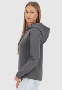 Grijze hoodie van zachte stof, met een trekkoordcapuchon, lange mouwen en ribgebreide manchetten, gecombineerd met lichtgewassen jeans.