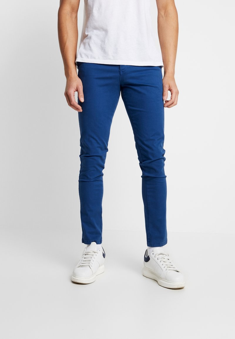 Modré slim-fit chinos vyrobené z bavlny, s hladkou texturou a bezšvovým designem. Doplněné bílými teniskami.