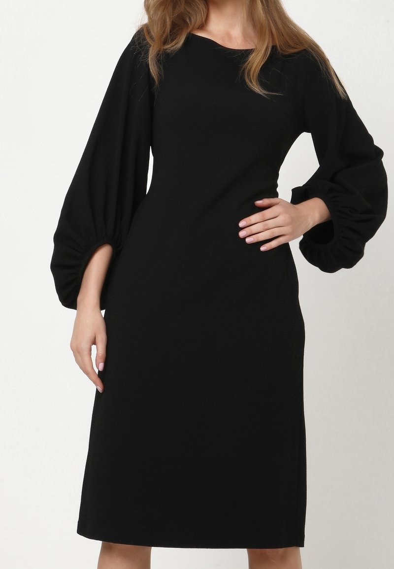 Robe noire en tissu doux, dotée de manches longues ballon et d'une coupe droite arrivant au genou, avec un col rond et sans ornements.