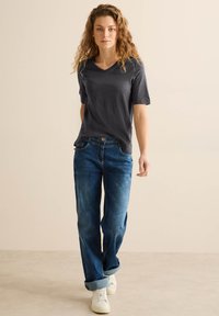 Grå v-hals t-shirt med korte ærmer, kombineret med løstsiddende blå jeans og hvide sneakers, med opbrettede manchetter og en afslappet silhuet.