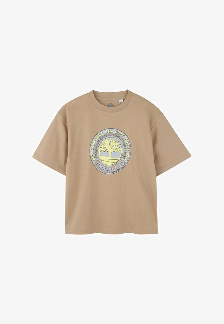 Lichtbruin T-shirt met korte mouwen, gemaakt van katoen. Bevat een cirkelvormig Timberland-logo met een boomontwerp in het midden en tekst eromheen.