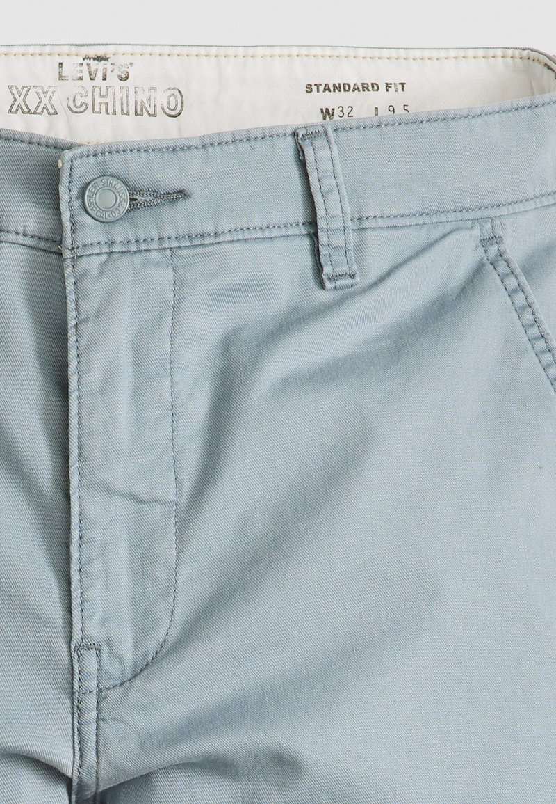 Chinos bleu clair en coton, avec une coupe standard, fermeture à bouton et poches latérales étroites avec de jolis détails de couture.
