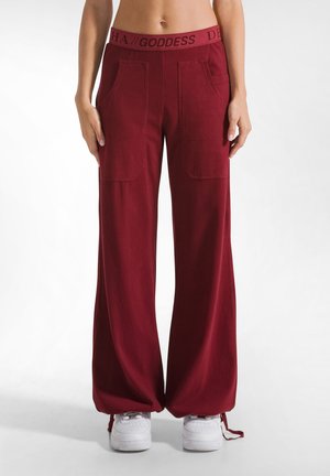Bordeaux wijde broek heeft een rekbare tailleband met de tekst "GODDESS", twee voorzakken en een gladde, zachte textuur.