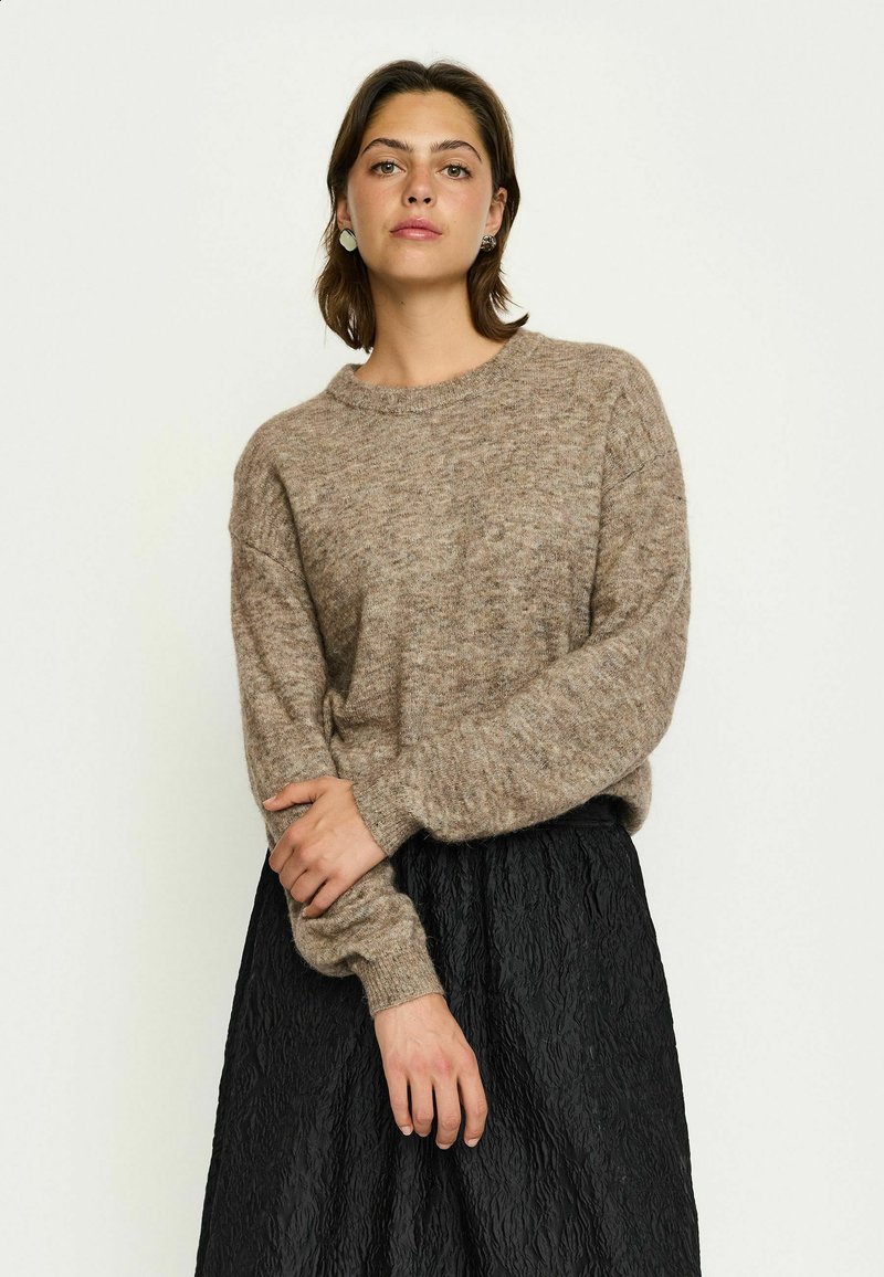 Pull en tricot beige avec un col rond et des manches longues, associé à une jupe noire texturée. Tons doux et atténués.