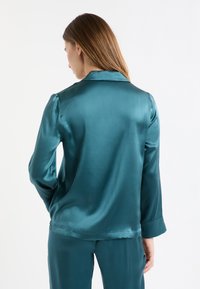 Conjunto de pijama de satén color verde azulado que incluye una camisa con cuello, mangas largas y puños abotonados, que muestra una textura suave, brillante y una caída elegante.
