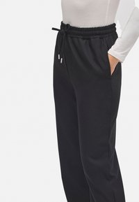 Pantalones jogger negros con cinturilla elástica ajustable, bolsillos laterales y textura suave, que se ajustan ligeramente en los tobillos.