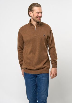 Brun zip-neck sweater med tekstureret strik, ribbenede manchetter og kant. Lille logo detalje på brystet, parret med blå jeans.