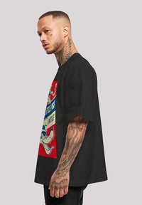 Černé oversized tričko s barevným grafickým potiskem kresleného vlka. Tkanina vypadá měkká; kulatý výstřih; krátké rukávy.