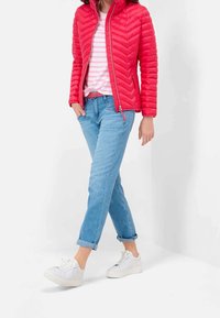 Chaqueta acolchada roja con patrón en forma de chevron, camiseta de rayas rosa y blanca, jeans de mezclilla azul claro enrollados, zapatillas blancas y cinturón a juego con los jeans.