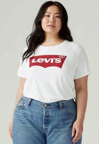 Wit T-shirt met korte mouwen en een groot rood Levi's-logo. Draagt met high-waisted blauwe spijkerbroeken, wat een casual outfit creëert.