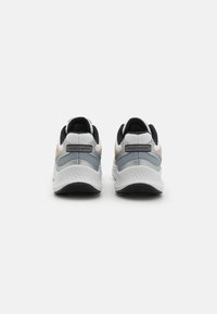 Baskets de sport blanches et noires avec une tige texturée, un design élancé, des accents gris et un logo visible sur le talon. Semelle en caoutchouc.