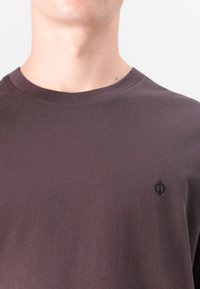 Dark purple cotton t-shirt with a round neckline and short sleeves. Features a small black embroidered logo on the left chest.