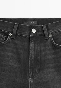 Zwarte denim jeans met een hoge taille, metalen knoopsluiting en subtiele slijtage-details bij de zakken. Merklabel zichtbaar.