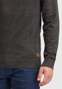 Tummanharmaa neulepaita, jossa on resorit hihansuissa ja helmassa. Alareunan vasemmassa kulmassa pieni ruskea nahkainen merkki. Sileä pinta ja vartalonmyötäinen istuvuus.