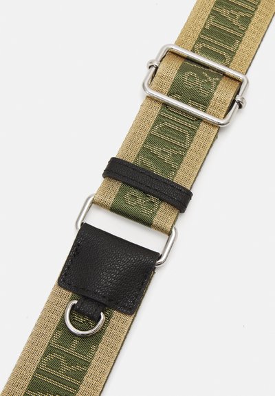 Sangle en toile beige avec lettrage vert, présentant un accent en cuir noir, des accessoires en métal argenté et des longueurs ajustables.