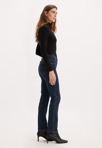 Jeans in denim scuro con una vestibilità classica, abbinati a un top aderente a maniche lunghe nero. Tacchi a punta neri completano il look.