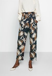 Luftiga, marinblå byxor med ett lövmönster i brunt och beige, med ett knyt i midjan, vida ben och fickor, som matchas med spetsiga vita klackar.