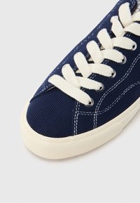 Σκούρο μπλε καμβά αθλητικό παπούτσι με λευκή δέσιμη κορδόνια, αντίθετη ραφή, υφασμάτινη υφή και στρογγυλή, μπεζ σόλα από καουτσούκ.