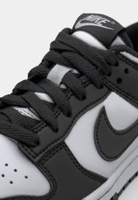 Black and white Nike sneaker with leather and textile material, featuring a lace-up design, visible stitching, and a logo on the tongue.