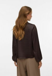 Blusa de satén marrón oscuro con mangas largas, puños abullonados y corte recto. Textura suave y diseño minimalista, vista desde atrás.