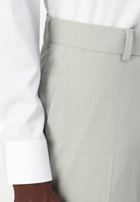 Šviesiai pilki kelnių, su tekstūruotu audiniu, su diržo kilpa, derinami su balta marškinių rankove su rankogaliu.
