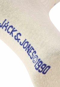 Beige sok med blåt "JACK & JONES 1990" tekst. Glat strikstruktur. Forlænget form der passer til fodtøj.