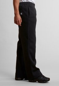 Sorte joggingbukser med afslappet pasform, elastisk talje og sidelommer. Fremstillet af blødt materiale med et logopatch på bagsiden.