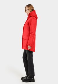 Röd, isolerad parka-jacka med huva, framdragkedja och sidofickor. Matchad med svarta jeans och kraftiga svarta kängor.