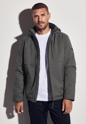 Donkergrijze, hooded jack met een gestructureerde afwerking, voorzien van twee borstzakken, lange mouwen en een ritssluiting aan de voorkant. Draag het over een wit shirt.