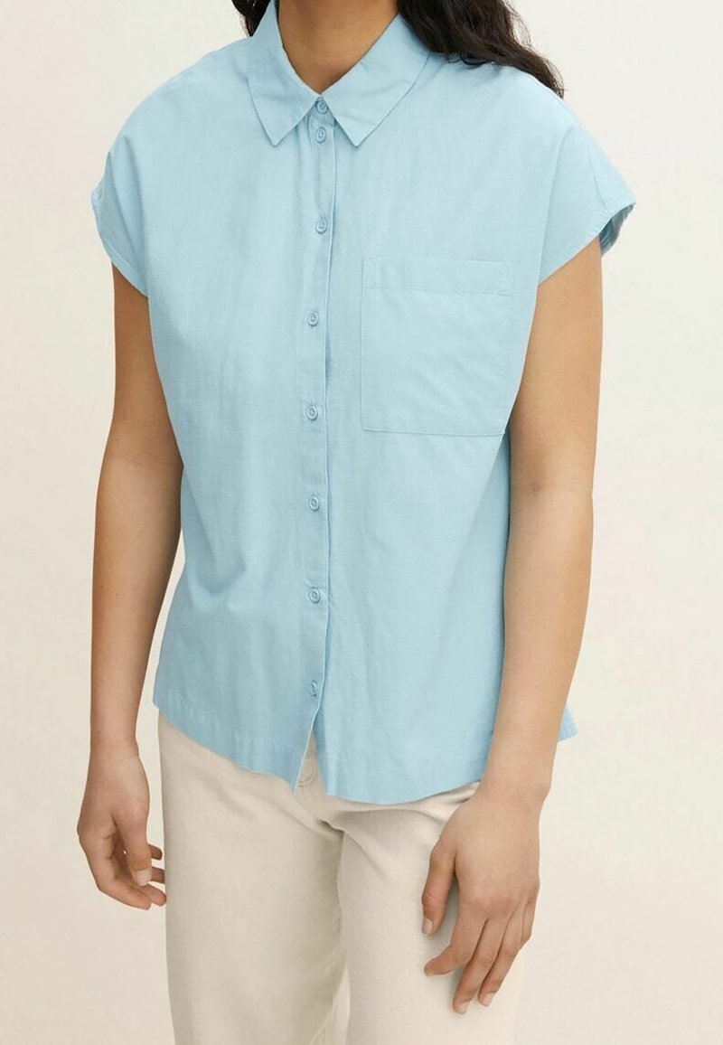Chemise bleu clair à boutons, avec col, manches courtes et poche poitrine. Fabriquée en tissu doux et texturé.