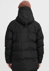 Sort polstret jakke med hætte, der har kviltet design, justerbar rem og en glat tekstur. Bagfra ses der ingen synlig branding.