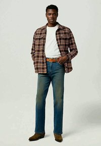 Ruudullinen paita ruskean ja kerman sävyissä, valkoinen T-paita, siniset farkut ja ruskea vyö. Malli pukeutunut ruskeisiin nilkkureihin; seisova poseeraus.