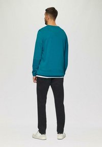 Türkisfarbener Rundhalspullover, schwarze Hose und weiße Turnschuhe. Der Pullover hat lange Ärmel und einen lockeren Schnitt, mit einer einfachen, glatten Textur.