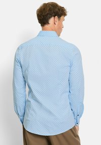 Light blue long-sleeve shirt with a small dot pattern, featuring a classic collar, button cuffs, and a curved hem. Smooth texture.